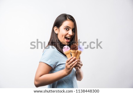Pretty young Indian/asian girl eating or presenting ice cream in cones, standing isolated over white background