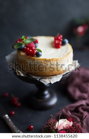 Homemade cheesecake with fresh berries on a dark wooden stand.