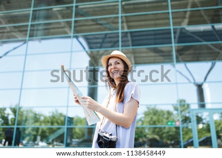 Young laughing traveler tourist woman with retro vintage photo camera holding paper map at international airport. Female passenger traveling abroad to travel on weekends getaway. Air flight concept