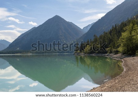 Coast line of a lake with trees and a mountain reflecting in calm water, picture from Austria.