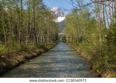 Little river with trees on both sides and a mountain top with snow in background, picture from Austria.