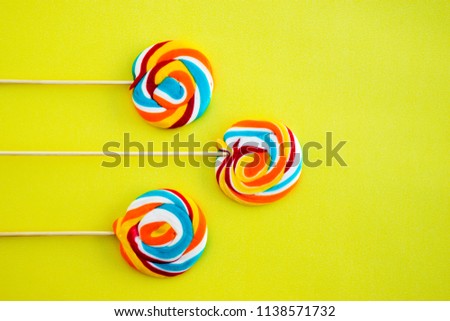 Colorful hard candy lollipop on yellow pastel background. Rainbow sweet pattern on stick flying around. Christmas holiday design concept elements.