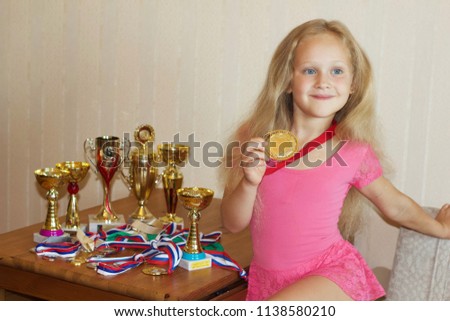 A nice little blonde blue-eyed girl gymnast champion with her medals and cups