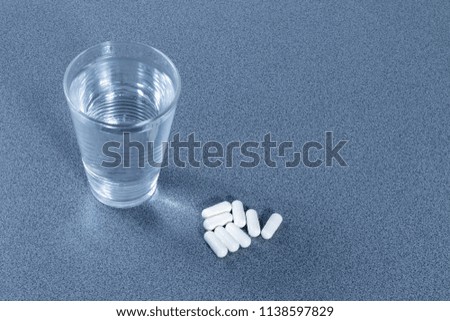 Some white tablets beside a glass full of water 