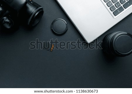 Work space on black table of photographer. Minimal workspace with Laptop, camera and lens copy space on dark background. Modern and elegant. Top view. Flat lay style.