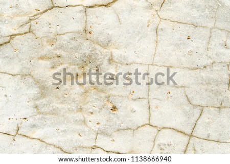 Texture of a light stone surface covered with cracks close up, background