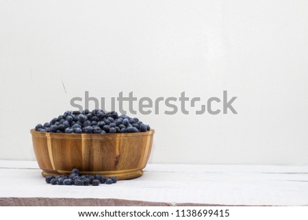 A wooden bowl full of fresh ripe blueberries just picked from the garden and set on a rustic white table top. A simple composition with lots of design space.