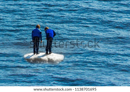 Two boys stand on a small white ice in the middle of the blue spring water.