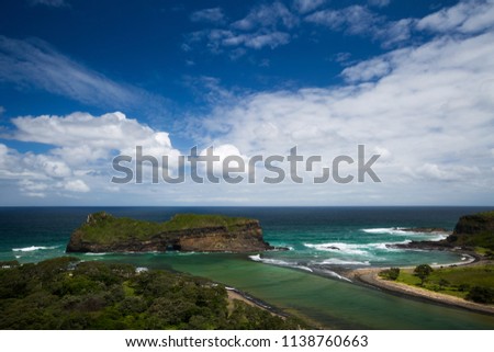 A landscape image of the Hole In The Wall landmark near Coffee Bay in the Wild Coast, Eastern Cape, South Africa. Ominous white clouds against a blue sky and turquoise sea water at the river mouth. Royalty-Free Stock Photo #1138760663