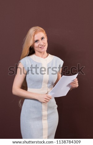 Young blonde woman in blue dress is holding paper in hands