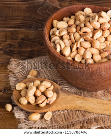 Dry roasted peanuts in a wooden bowl and spoon on a burlap cloth and wood surface