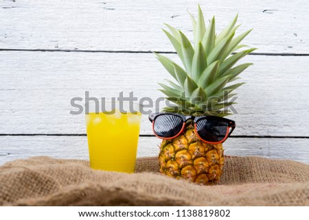 whole ripe pineapple and Cold juice with sunglasses and headphone listens to music on sack and white wooden background.