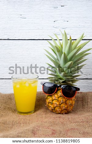 whole ripe pineapple and Cold juice with sunglasses and headphone listens to music on sack and white wooden background.