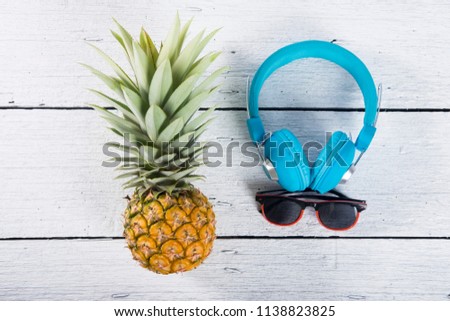 whole yellow pineapple with sunglasses and headphone on white wooden background.