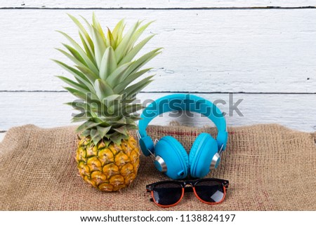cute ripe pineapple with sunglasses and headphone on white wooden background.