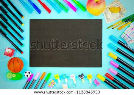 black board on blue background surrounded by stationery and recreation objects representing back to school