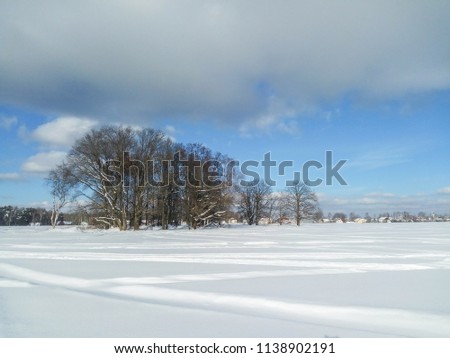 Vast countryside expanse, covered by abundant snow blanket under cloudy blue sky.
