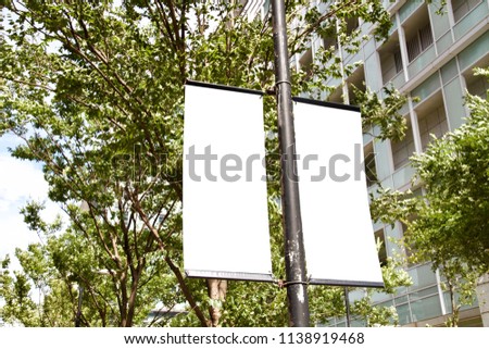 The blank advertising banner suspended on the street lamp pole with the tree and building facade background.
