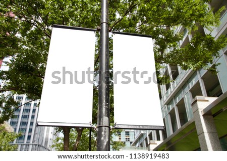The blank advertising banner suspended on the street lamp pole with the tree and building facade background. Royalty-Free Stock Photo #1138919483