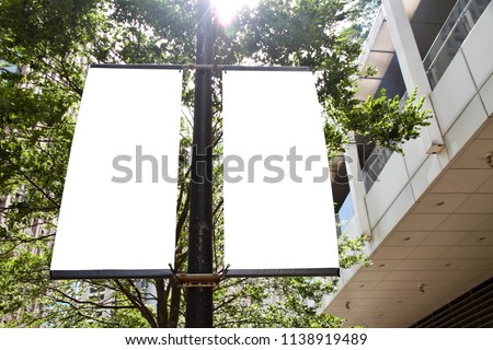 The blank advertising banner suspended on the street lamp pole with the sunlight from the tree background.
