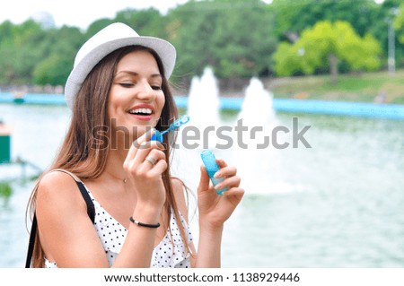 Young cheerful woman in a white hat blowing soap bubbles in a park in the background of a lake