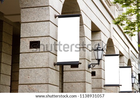 A series of vertical blank advertising mockup of placards are suspended on the facade of the vintage marble  European styled architecture.