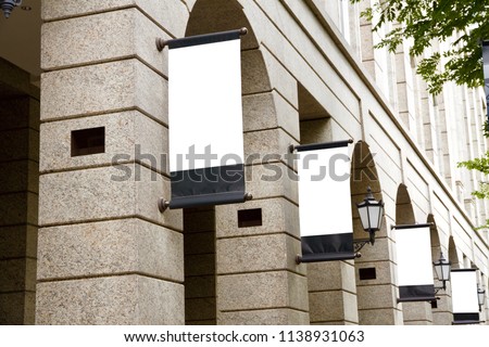 A series of vertical blank advertising mockup of placards are suspended on the facade of the vintage marble  European styled architecture.