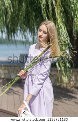 Beautiful young model on the shore of the lake. The girl is blonde in a purple dress with a backpack in her hand