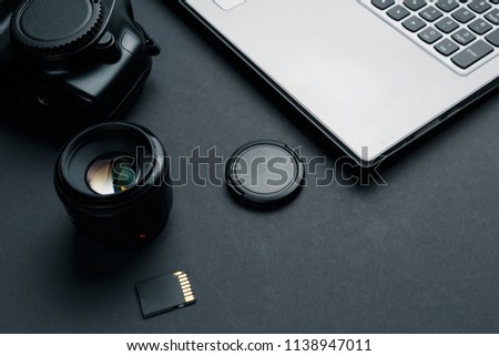 Work space on black table of photographer. Minimal workspace with Laptop, camera and lens copy space on dark background. Modern and elegant.