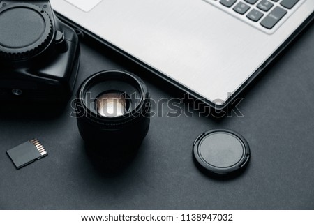 Work space on black table of photographer. Minimal workspace with Laptop, camera and lens copy space on dark background. Modern and elegant.