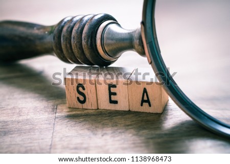 Vintage Magnifying Glass Leaning Over SEA Blocks On An Old Wooden Table - Search Engine Advertising Concept