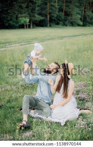 father with mother raises baby on hands resting on a picnic in the nature