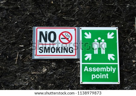 No smoking  and a assembly point here sign on a black background UK