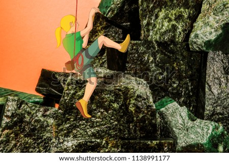Ascending strong blonde female climber to the top of jade mountains on orange background