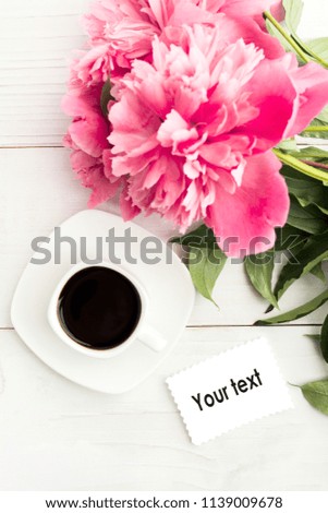 Pink peony flowers with white cup of coffee with note of your isolated text over wooden background. Woman's or Mother's day concept, vertical shot