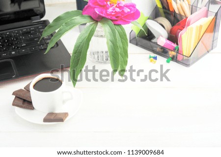 Coffee break with chocolate on working place at home with peony, laptop, stationery. Freelance concept with copy space on wooden table