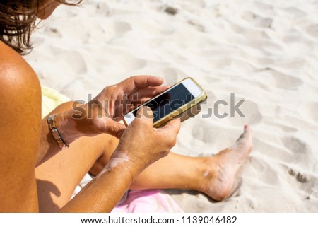 Woman with vitiligo on her hands is using a phone and gets suntanned on the beach  Royalty-Free Stock Photo #1139046482