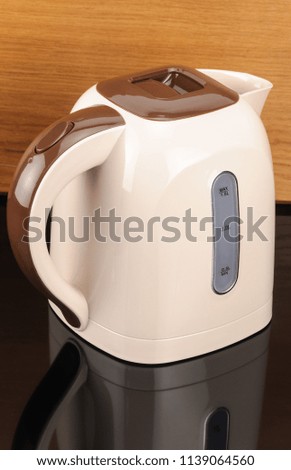 Beige and brown color plastic cordless electrical kettle on the wood and black mirror background