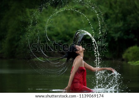 Asian woman relaxing and enjoying playing with water and splash at tropical exotic river with turquoise amazing color water in beautiful destination forest. Travel Concept
