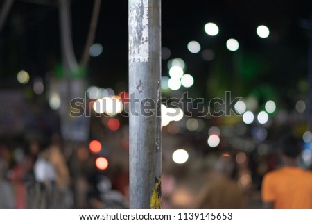 Dirty street pole with stickers and markings in a busy Indian market street at night with bokeh background, city nightlife