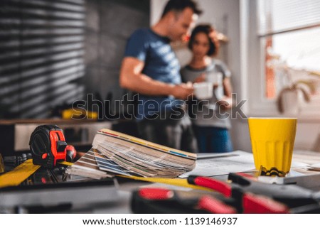 Picture of color swatch with tape measure on the table in the kitchen with couple standing in the background