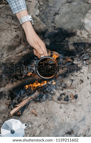 Girl's hand holds the cup coffee on the background of the fire . Adventure, travel, tourism and camping concept. 