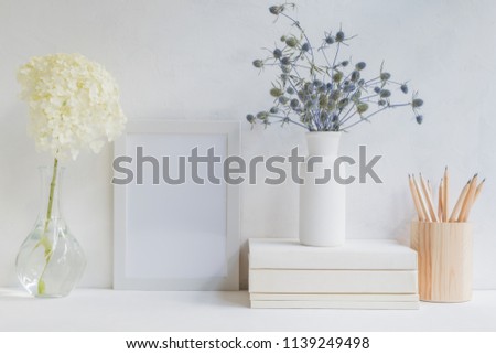 Home interior with decor elements. White frame, flowers in a vase, books and pencils