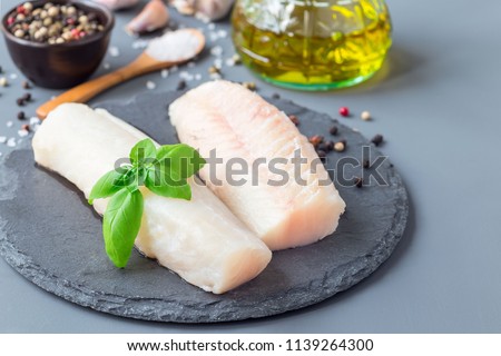 Fresh raw cod fillet with spices, pepper, salt, basil on a stone plate, horizontal, copy space