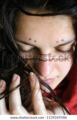photo portrait of a wild girl with ethnic patterns on her face in red clothes wet dark hair inhales with her eyes closed