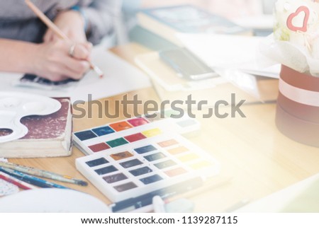 Pretty smiling young woman drawing a picture with poster paint. Front view on drawing girl with palette in her hand. Smiling young woman draw a picture at studio