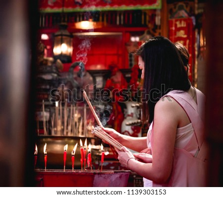 Perspective view of a Chinese woman perform her prayer inside red Buddha temple by burning incense sticks.