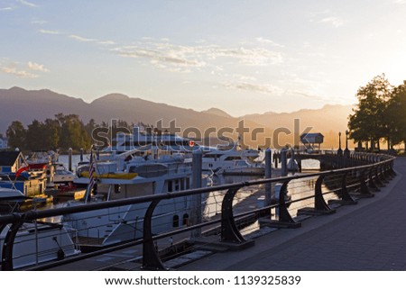 A broad walkway along Coal Harbour marina at sunrise in Vancouver BC, Canada. Harbor landscape with vessels and mountain ridges on the horizon.