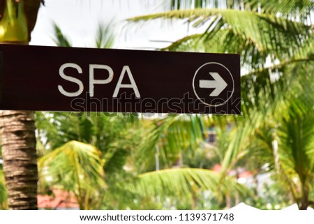 SPA. The inscription on a wooden dark board. The arrow indicates the direction. Pointer on the background of palm trees