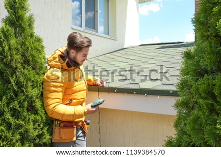 Young man decorating roof with Christmas lights